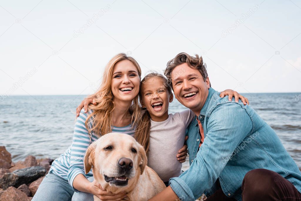 Family with golden retriever looking at camera while embracing on beach 