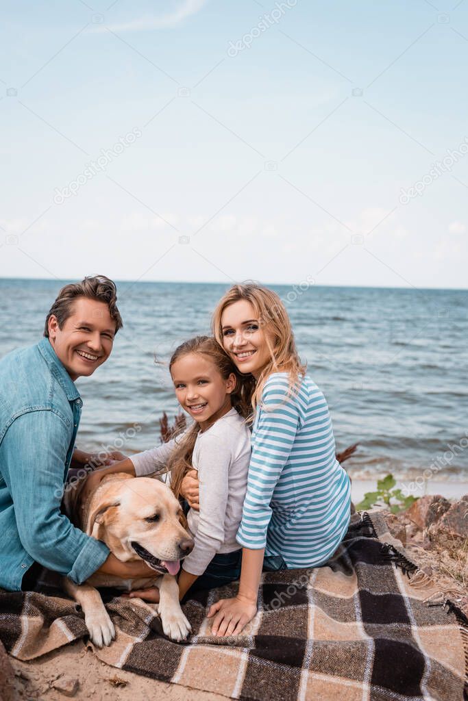 Family with golden retriever looking at camera while sitting on blanket 