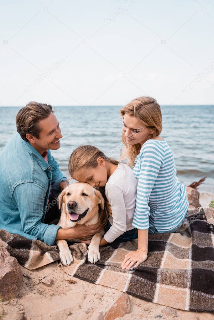 Man petting golden retriever near wife and daughter on beach 