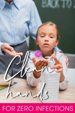 Okullu kızın öğretmeninin yanına el dezenfektanı sürmesi ve sınıfta enfeksiyon kapmaması için temiz eller kullanması. 