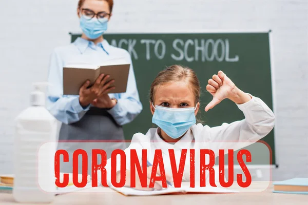 Tıp maskesinin seçici odak noktası baş parmağını aşağı gösteren, tahtaya yakın tahtada elinde Coronavirus harfleriyle duran öğretmen. 