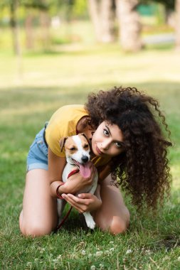Çimenlerde oturan ve köpeği kucaklayan genç bir kadının seçici odağı.