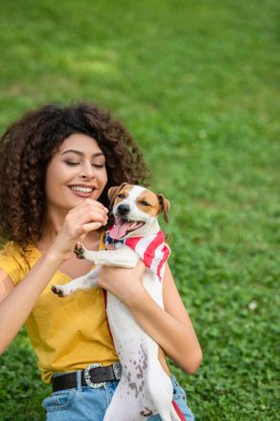 Amerikan bandanasıyla oturan ve köpeği tutan genç bir kadının seçici odak noktası.