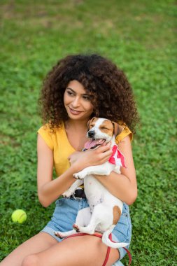 Seçici odak noktası, genç bir kadının köpekle çimenlerde oturması ve başka tarafa bakması.