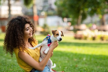 Amerikan bayrağı bandanasında çim üzerinde köpekli genç bir kadının seçici odağı