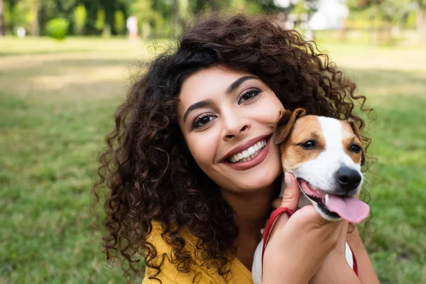 Neşeli kadının seçici odağı kameraya bakıyor ve köpeği tutuyor.