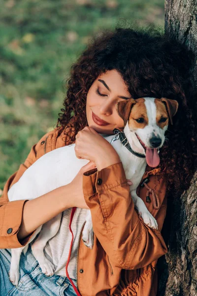 Wanita Muda Berjas Hujan Memeluk Jack Russell Terrier Dekat Pohon — Stok Foto