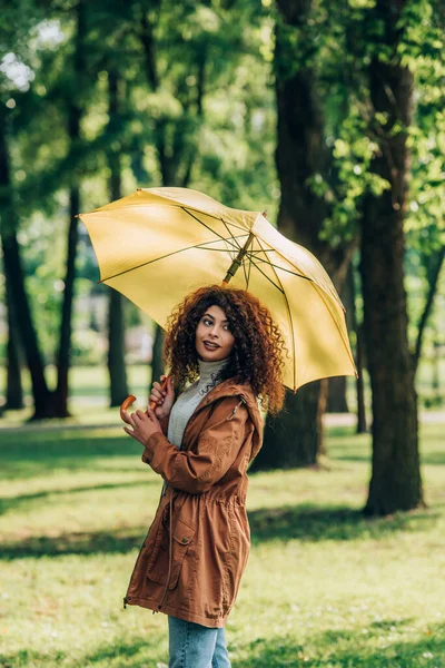 穿着雨衣的年轻女子拿着雨伞在公园里 — 图库照片