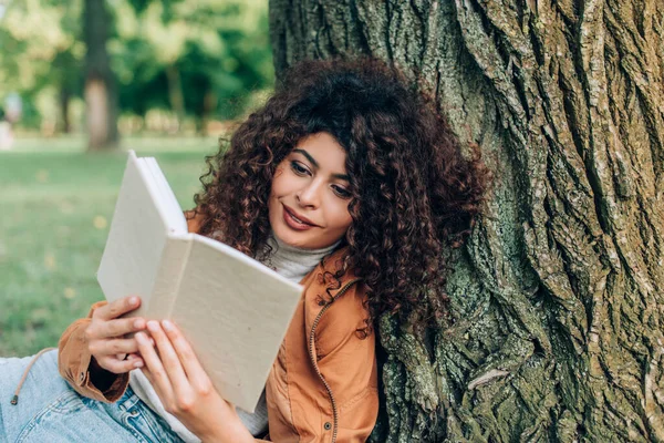 Молодая Кудрявая Женщина Читает Книгу Возле Дерева Парке — стоковое фото