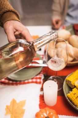 cropped view of senior man pouring white wine into glass during thanksgiving dinner clipart