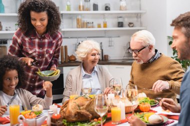 Şükran Günü 'nde, bayram yemeğinde sebze servis eden neşeli Afro-Amerikan kadınlarının seçici odağı.