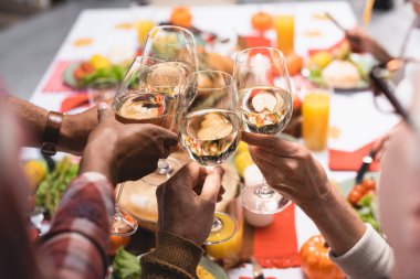 partial view of multiethnic relatives clinking wine glasses while celebrating thanksgiving day clipart