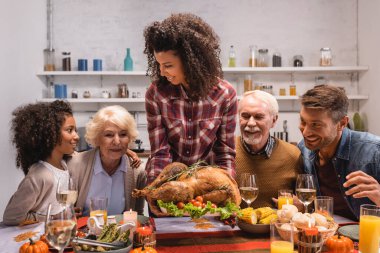 Seçici odak noktası, Afrika kökenli Amerikalı bir kadının ailesinin yanında lezzetli bir hindi ve masa süsleri tutması. 