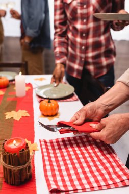 Çok ırklı bir ailenin şükran günü kutlaması sırasında masanın yanında çatal bıçak taşıyan yaşlı bir kadın görüntüsü. 