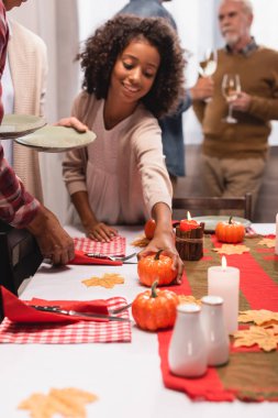 Afrika kökenli Amerikalı çocuğun Şükran Günü kutlamaları sırasında ailenin yanındaki masaya dekoratif balkabağı koymasının seçici odağı. 