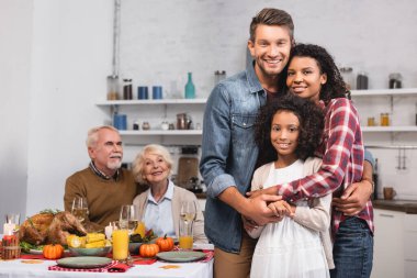Kızı şükran günü kutlaması sırasında kameraya bakan çok ırklı ebeveynlerin seçici odağı 