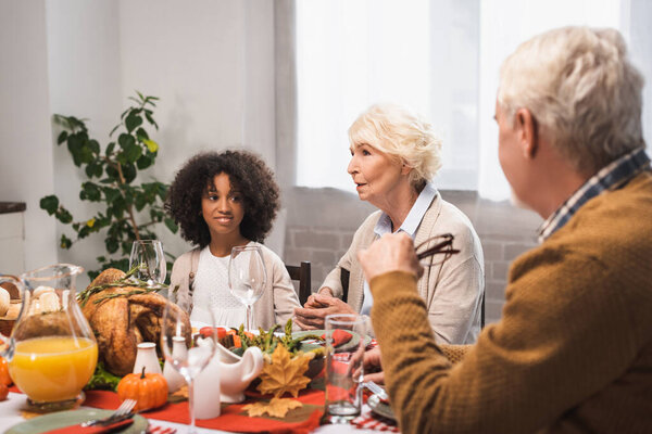 selective focus of senior woman talking to multicultural family during thanksgiving dinner