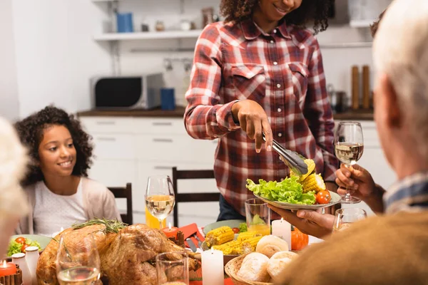 在感恩节宴会上把蔬菜放在盘子里的美国黑人妇女 — 图库照片