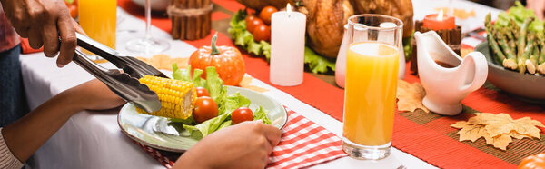 cropped view of mother putting corn on plate near daughter during thanksgiving dinner, website header