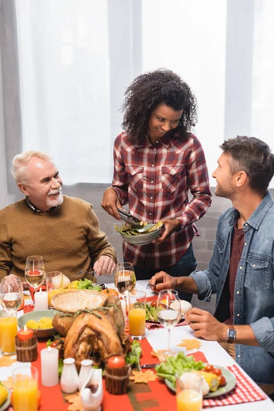 Afro-Amerikalı kadın elinde kuşkonmaz tabağıyla bir adama bakıyor.
