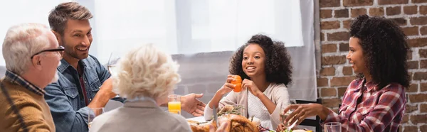 感恩节大餐期间 多文化家庭坐在美味火鸡旁边的全景照片在桌上 — 图库照片