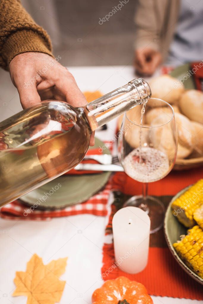 cropped view of senior man pouring white wine into glass during thanksgiving dinner