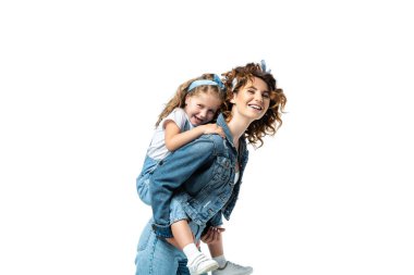 side view of laughing mother piggybacking daughter in denim outfit isolated on white clipart