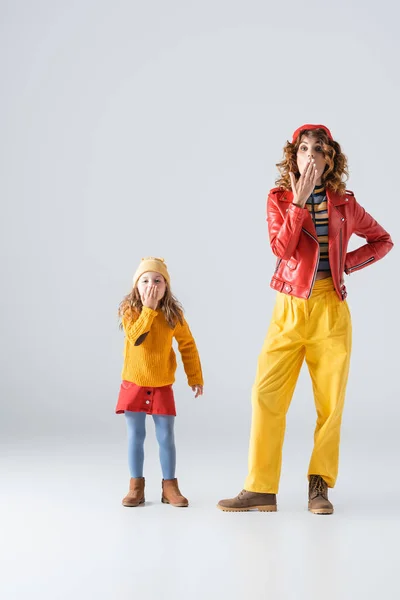 ショックを受けた母親と娘のカラフルな赤と黄色の衣装は灰色の背景に口を覆う — ストック写真