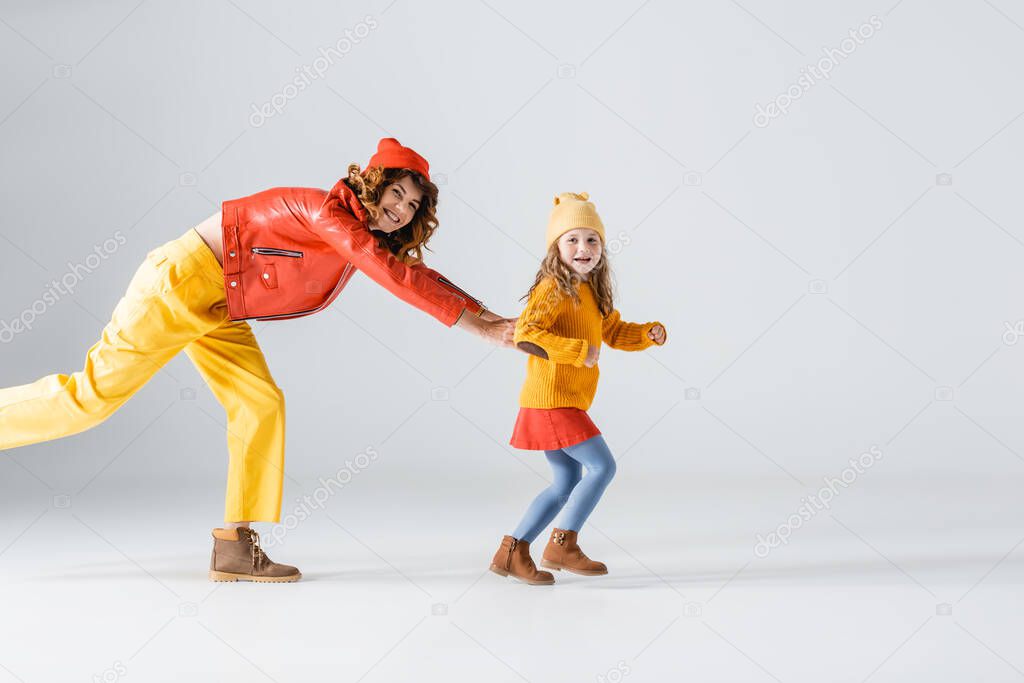 side view of mother and daughter in colorful red and yellow outfits running on grey background