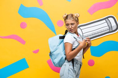 Sarı arka planda kağıt kalem ve soyut elementlerle sırt çantasına bakan şok olmuş öğrenci.