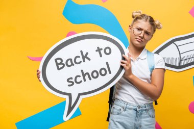 Elinde konuşma balonu, elinde kağıt kalem ve sarı renkli elementlerle okula geri dönen liseli kız.