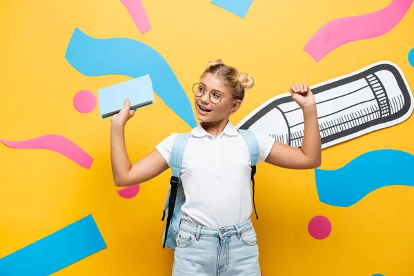 Excited Schoolgirl Eyeglasses Holding Book Showing Triumph Gesture Paper Pencil — Stock Photo, Image