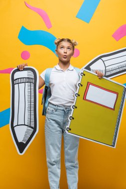 Sarı arka planda kağıt sanatının yanında kağıt kalem ve defter tutan düşünceli bir kız.