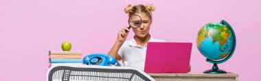 Liseli kızın laptopun, dünyanın ve pembe üzerine izole edilmiş kitapların yanında loupe 'u tutarken panoramik görüntüsü. 