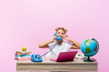 Akıllı telefondan konuşan okul çocuğu, kitapların yanında telefon ve pembe renkte izole edilmiş dünya. 
