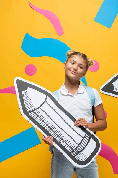 Schoolkid Κοιτάζοντας Την Κάμερα Ενώ Κρατώντας Μολύβι Χαρτί Κίτρινο Φόντο — Φωτογραφία Αρχείου