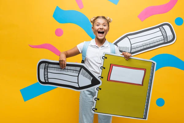 Opgewonden Schoolkind Met Papier Potlood Notebook Gele Achtergrond — Stockfoto