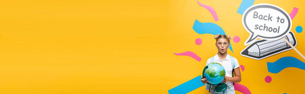 Panoramic shot of excited schoolchild with globe standing near paper art on yellow background