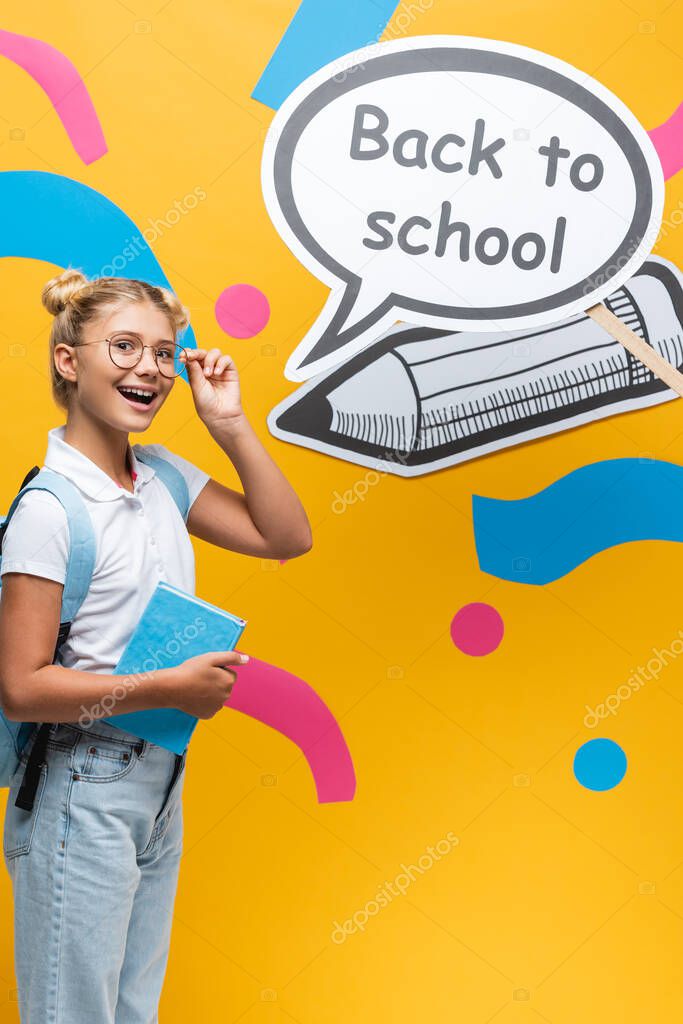 Schoolkid with backpack and eyeglasses standing beside speech bubble with back to school lettering and paper craft on yellow background