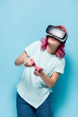 KYIV, UKRAINE - 29 Temmuz 2020: Mavi arka planda joystick ile video oyunu oynayan pembe saçlı genç kadın
