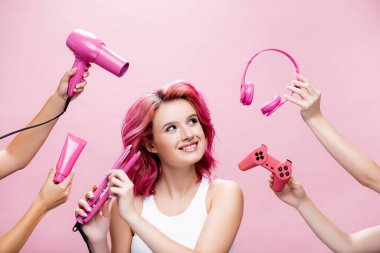 KYIV, UKRAINE - 29 Temmuz 2020: Kulaklık, kozmetik kremi, joystick ve saç kurutma makinesi kullanan, pembe ellerde bulunan renkli saçlı genç kadın