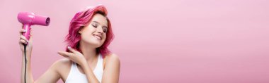Pembe panoramik çekimde izole edilmiş saç kurutma makinesi kullanan renkli saçlı genç bir kadın.