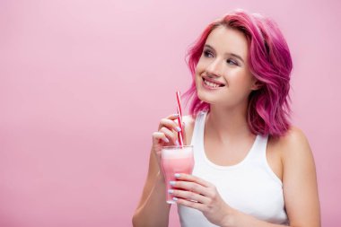 Renkli saçlı, çilekli milkshake 'i tutan ve pembe üzerinde saman içen genç bir kadın.