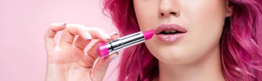 cropped view of young woman with colorful hair holding lipstick isolated on pink, panoramic shot clipart