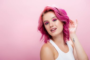 Renkli saçlı ve makyajlı genç bir kadın pembe üzerinde yalnız poz veriyor.