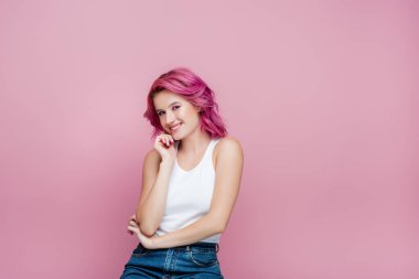 Renkli saçlı genç bir kadın pembe üzerinde izole bir şekilde gülümsüyor.