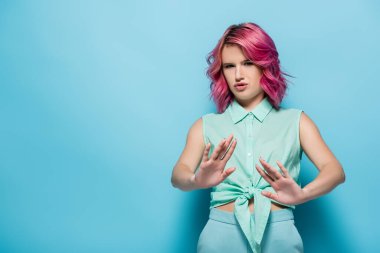 confused young woman with pink hair showing refusal on blue background clipart