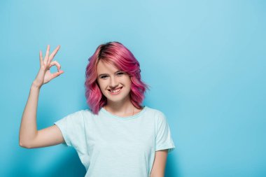 young woman with pink hair showing ok sign on blue background clipart