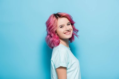 side view of young woman with pink hair smiling on blue background clipart