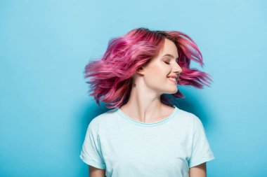 Genç bir kadın mavi arka planda pembe saç sallıyor.